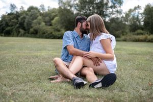 A couple sitting close together on grass in a peaceful outdoor setting.