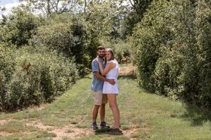A couple standing together on a path through an orchard on a sunny day.