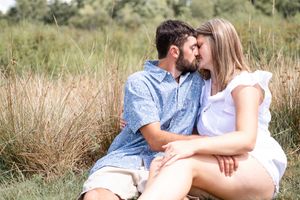 A couple in white and blue outfits sharing an intimate moment in tall grass.