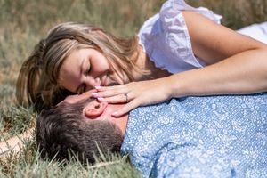 A couple lying in grass sharing a playful intimate moment together.