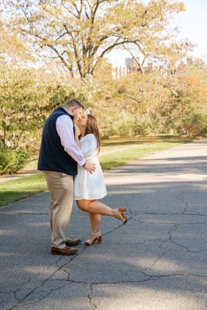A romantic couple embraces on a tree-lined path during an autumn engagement photoshoot.
