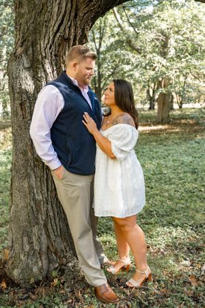 A couple shares an intimate moment against a large tree trunk during their engagement session.
