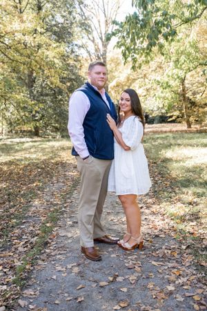 A couple poses for engagement photos on a leaf-covered path during fall.