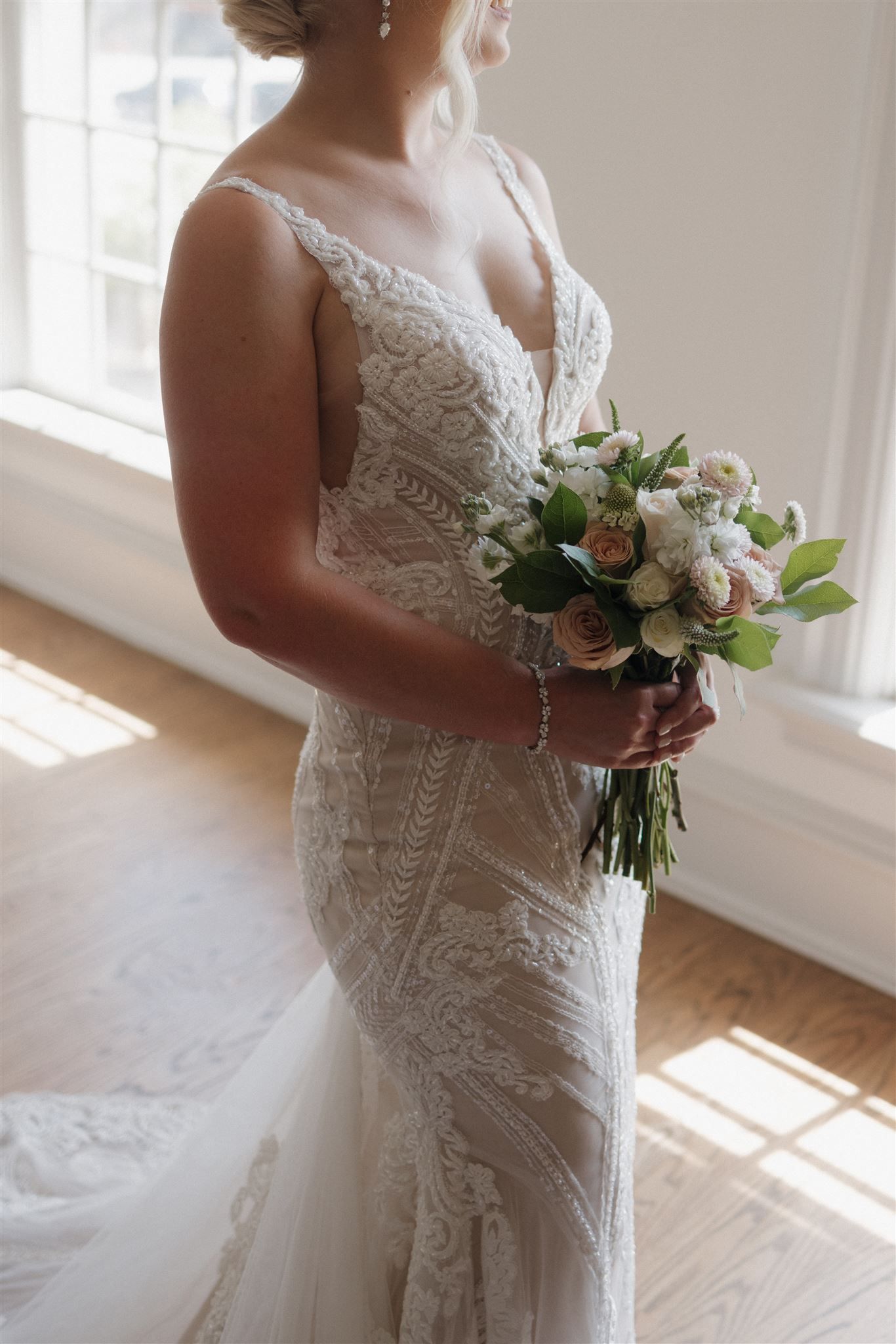 Close-up of a fitted lace wedding gown with delicate beading and white floral bouquet.