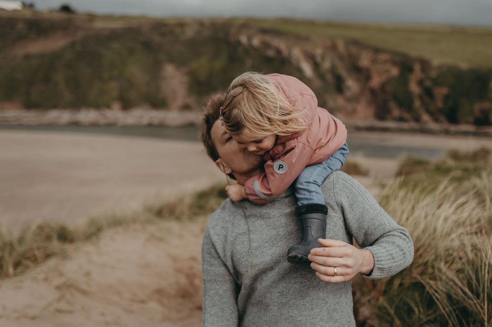 Tender embrace between family members against coastal cliff backdrop.