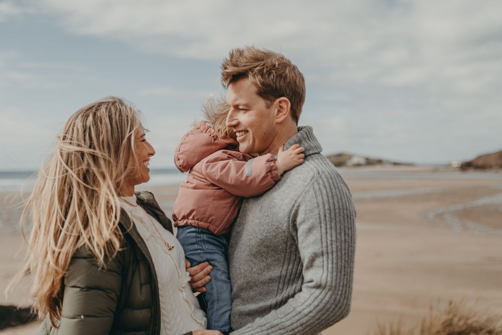 Intimate family moment captured during seaside photo session on cloudy beach day.