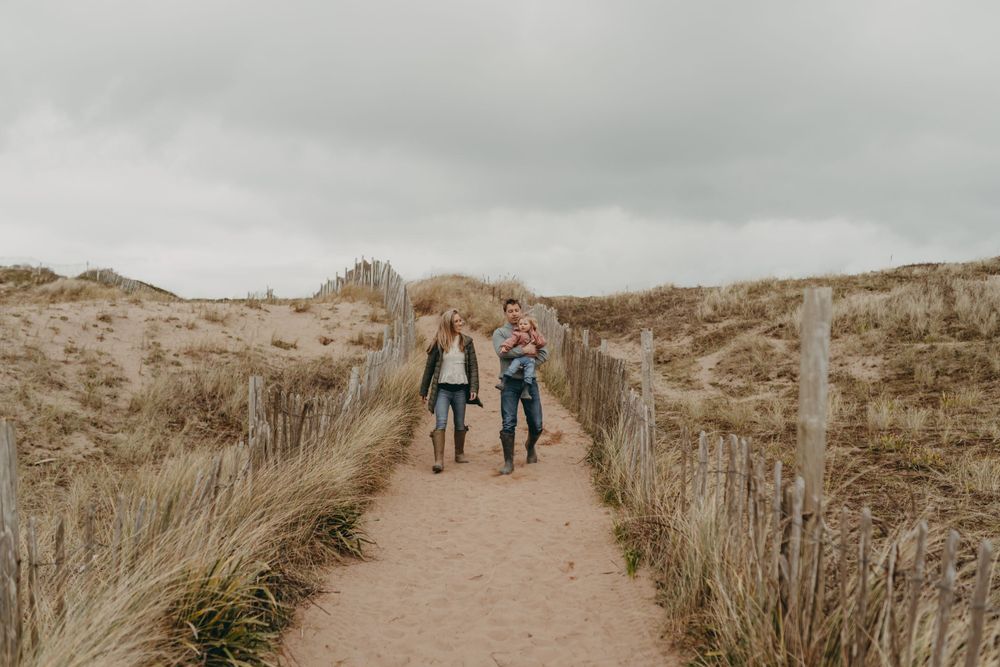 Couple walking along a winding sandy path through coastal dunes.