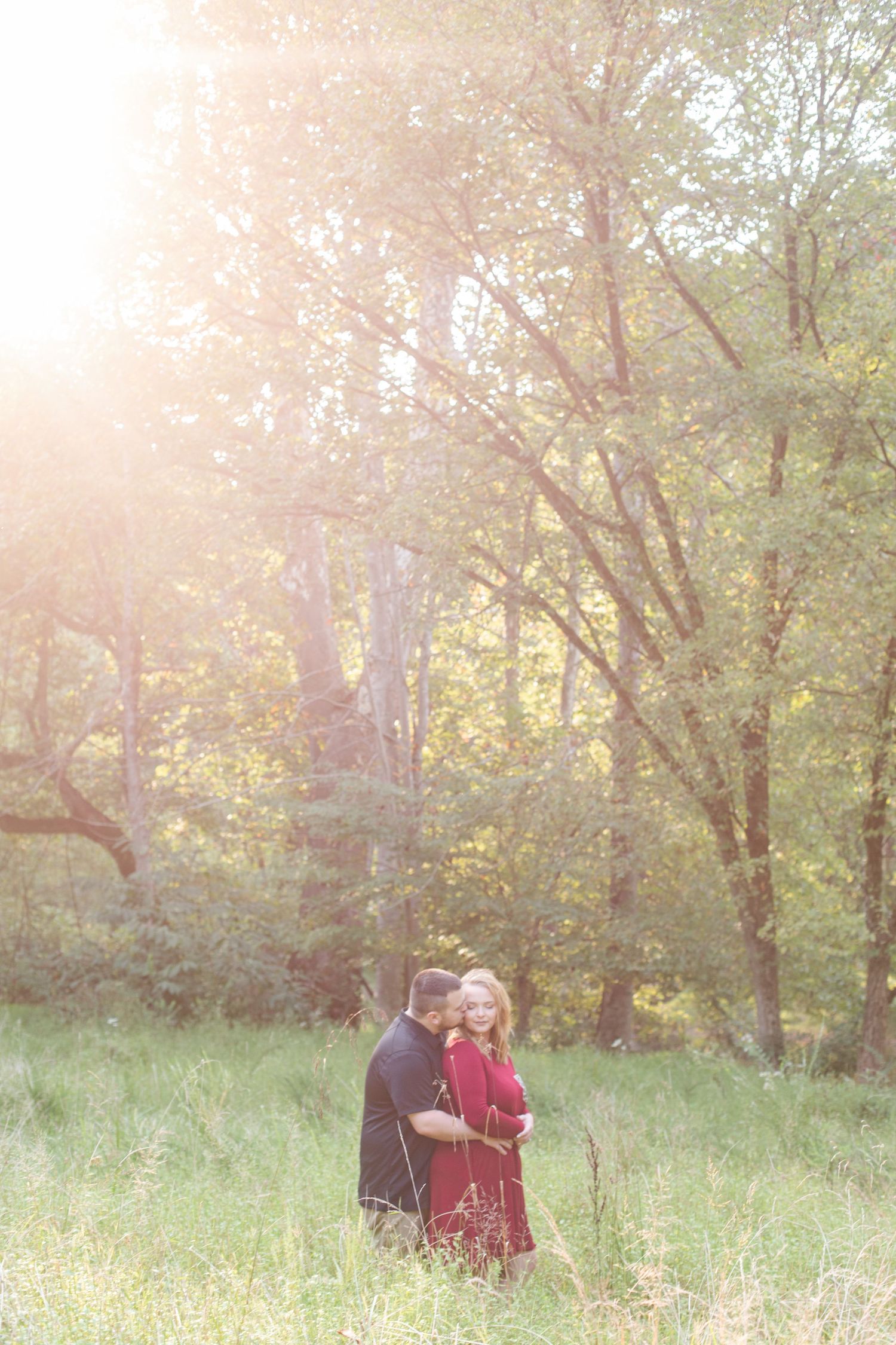 Romantic outdoor photoshoot in a wooded area with golden sunlight filtering through the trees.