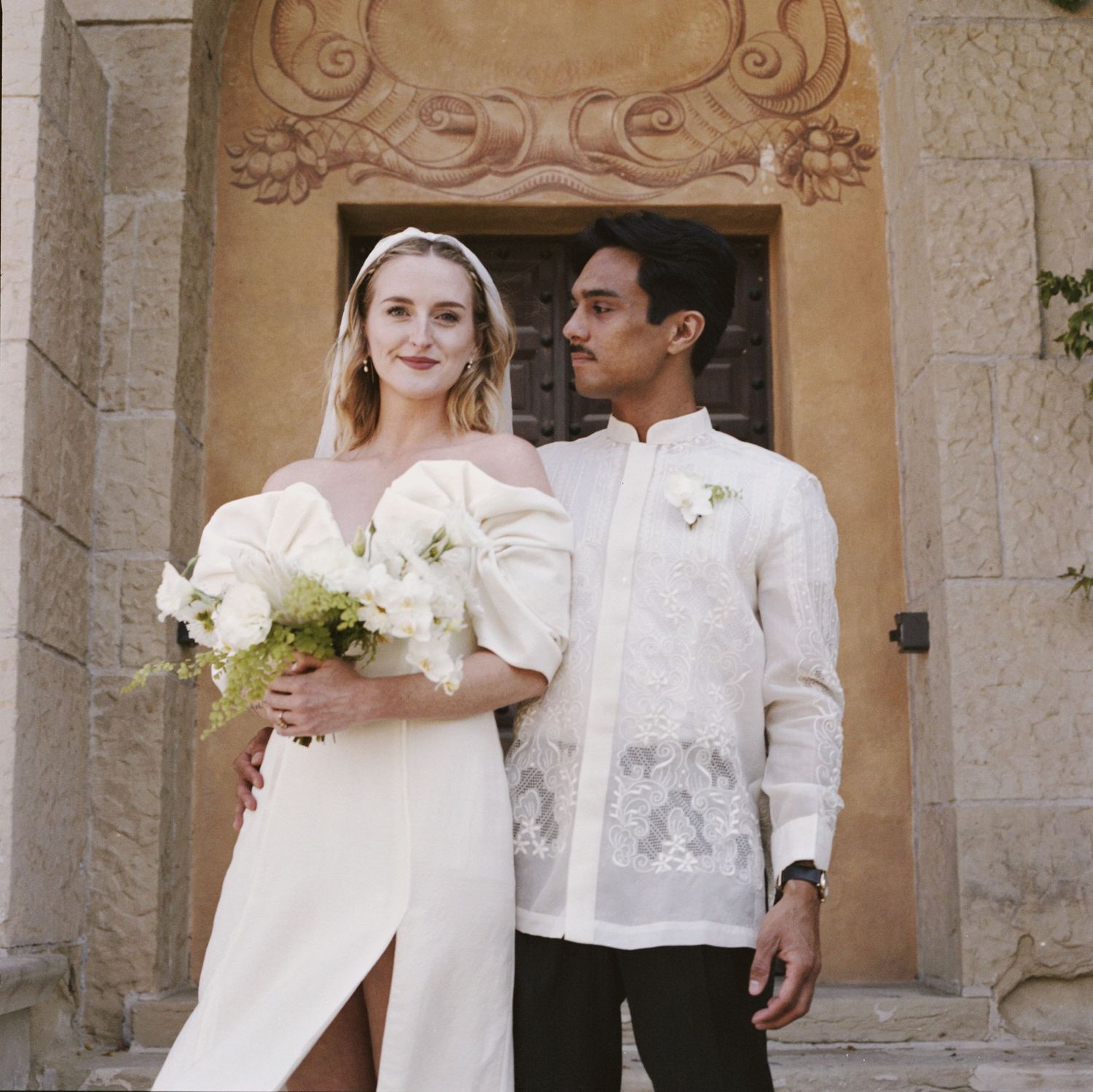 Bride and groom pose elegantly in front of a Spanish colonial archway.