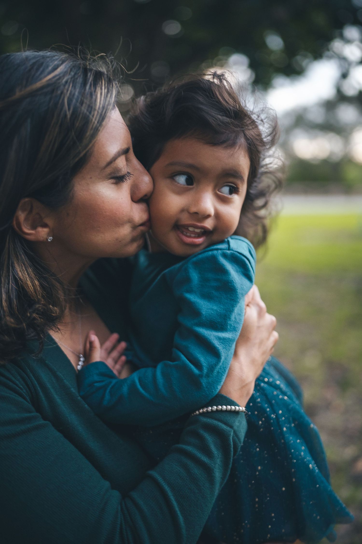 Tender moment captured between parent and child in teal clothing outdoors.