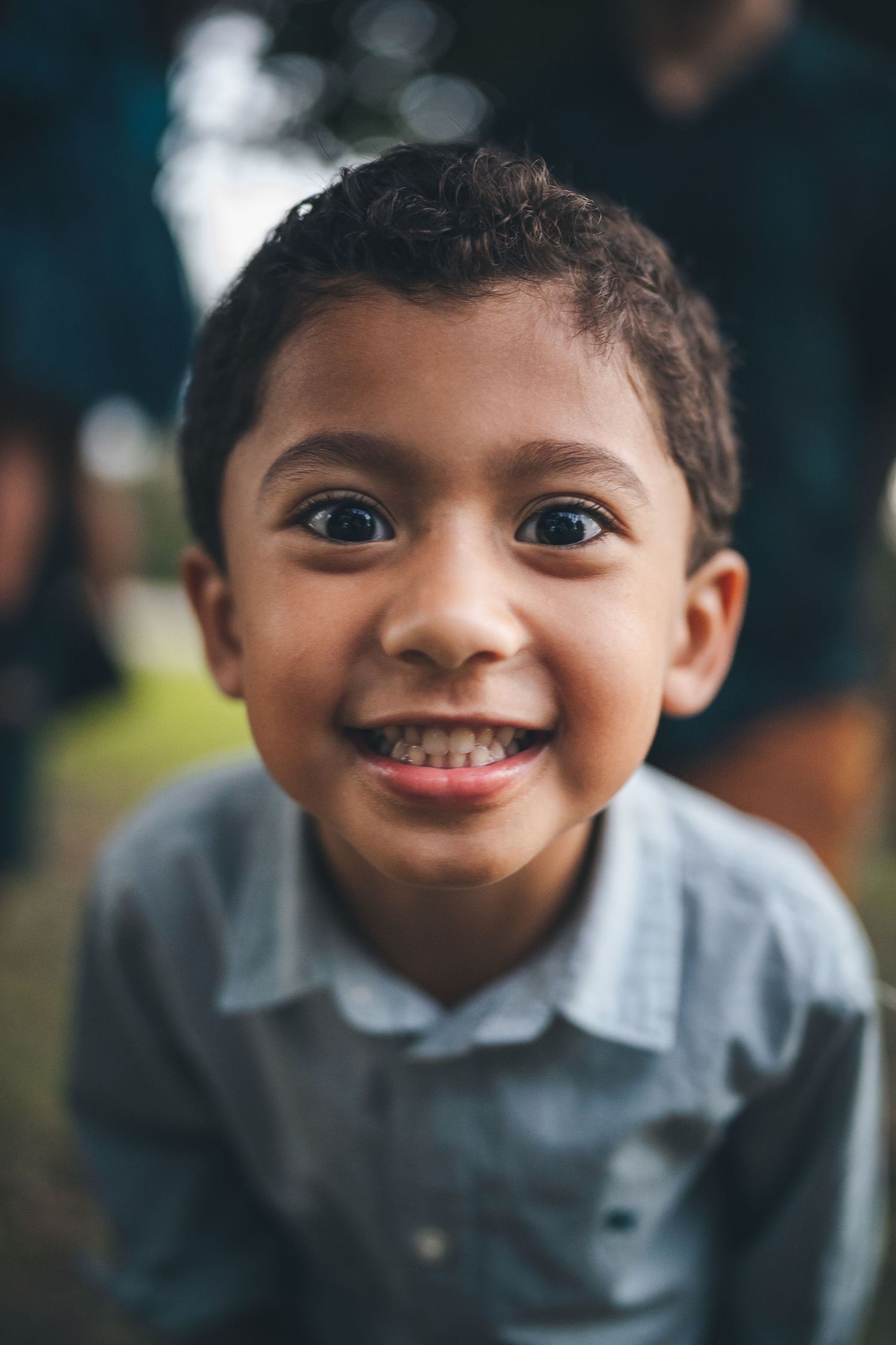 Close-up portrait of young child in gray shirt with bright smile outdoors.