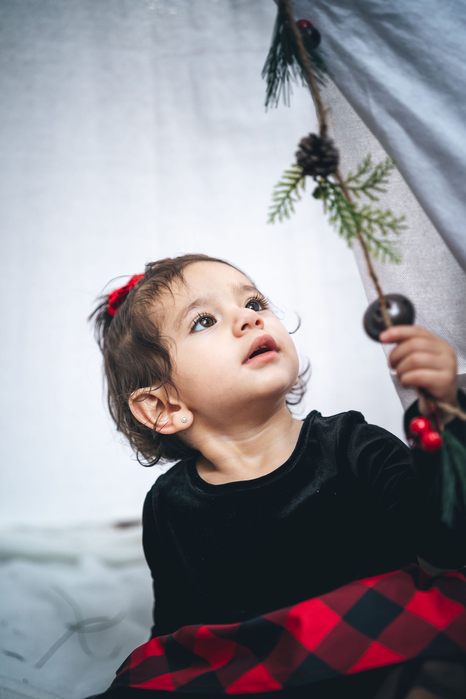 Small child in black top looks up at pinecone decoration hanging inside teepee.