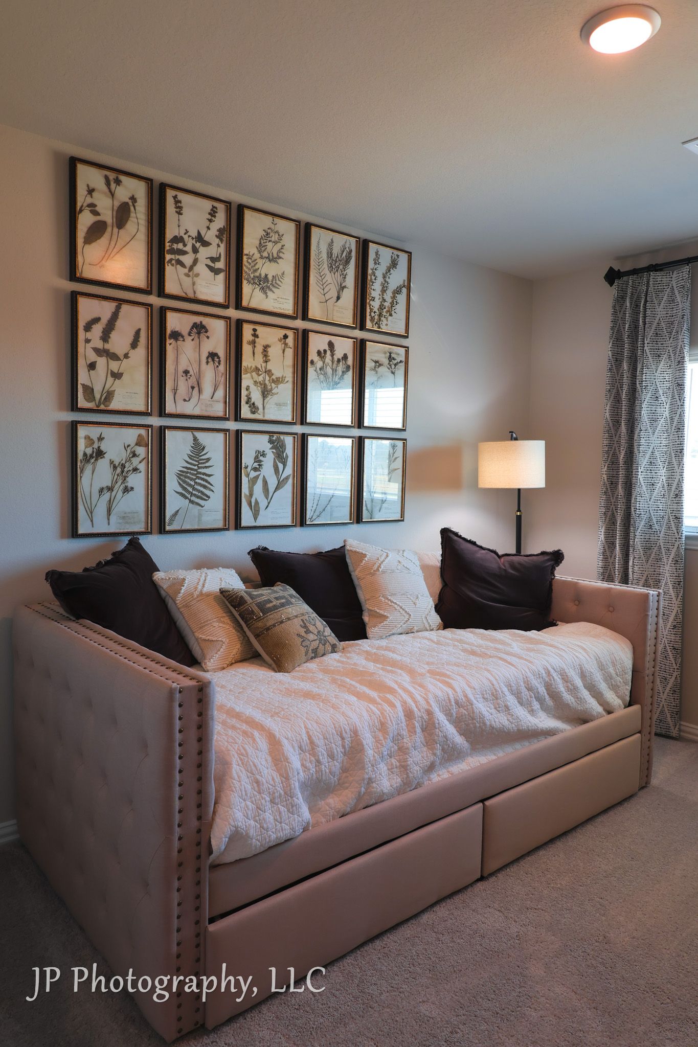 Stylish daybed with botanical gallery wall and throw pillows in neutral toned room.