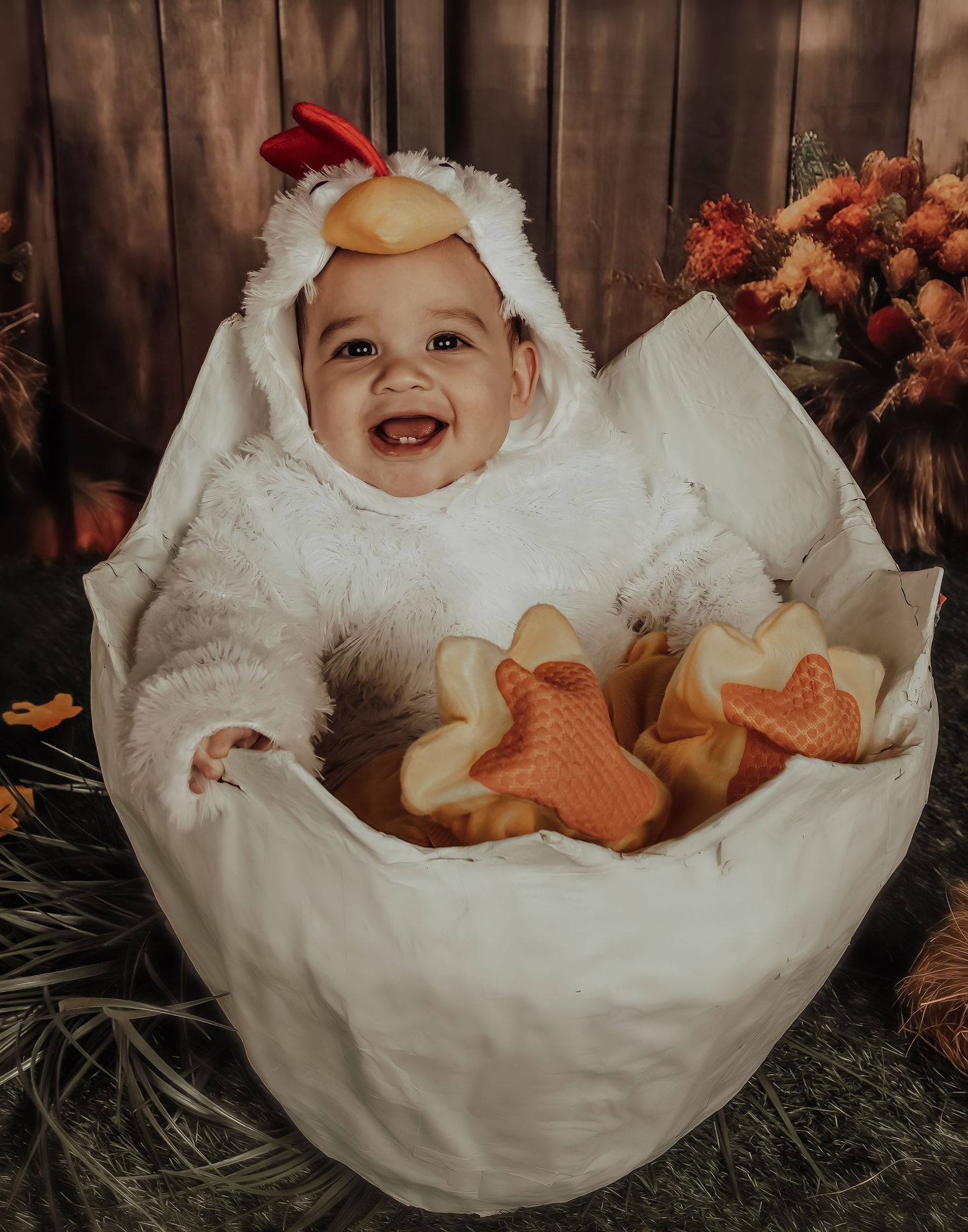 A whimsical baby chicken costume portrait with fall decorations and a rustic wooden background.