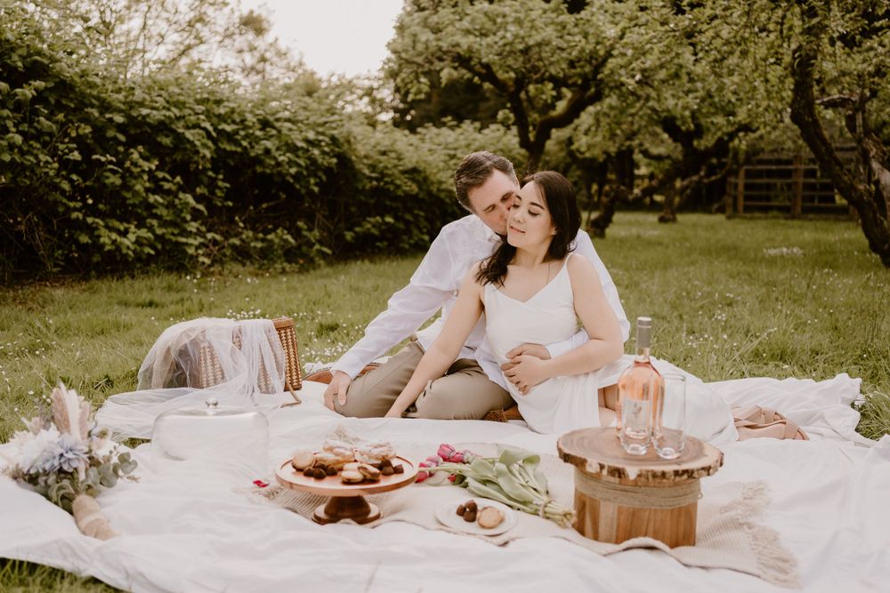 A romantic picnic setup on a white blanket in a grassy field with pastries and treats.