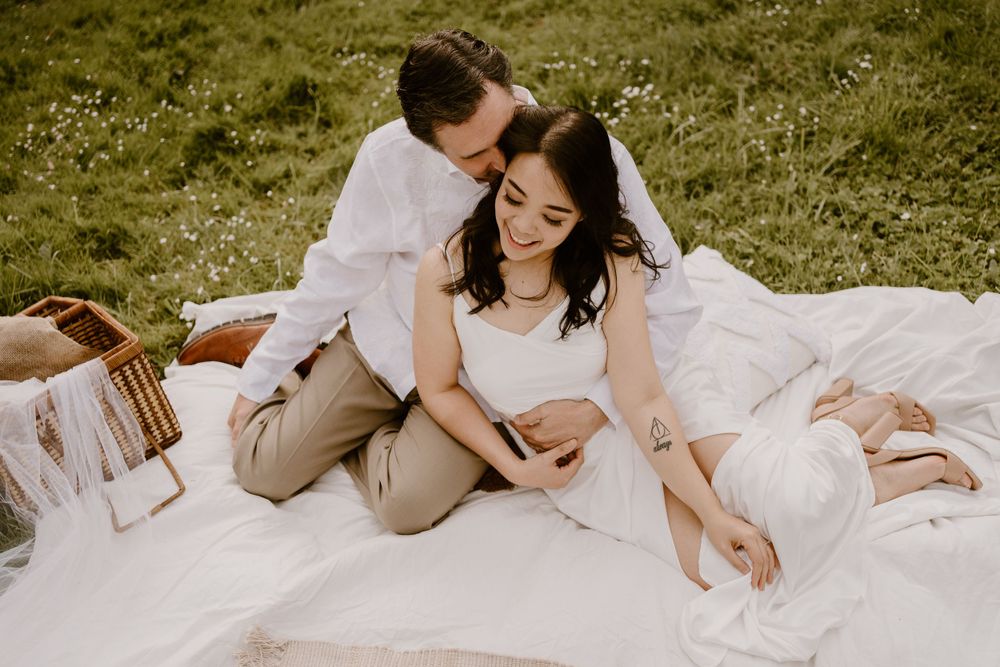Couple lounging together on a white picnic blanket in a sunny meadow.