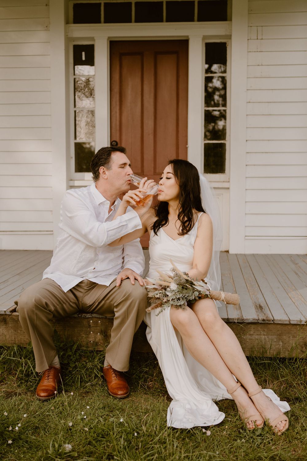 A couple shares playful moments on a white farmhouse porch with wooden details.