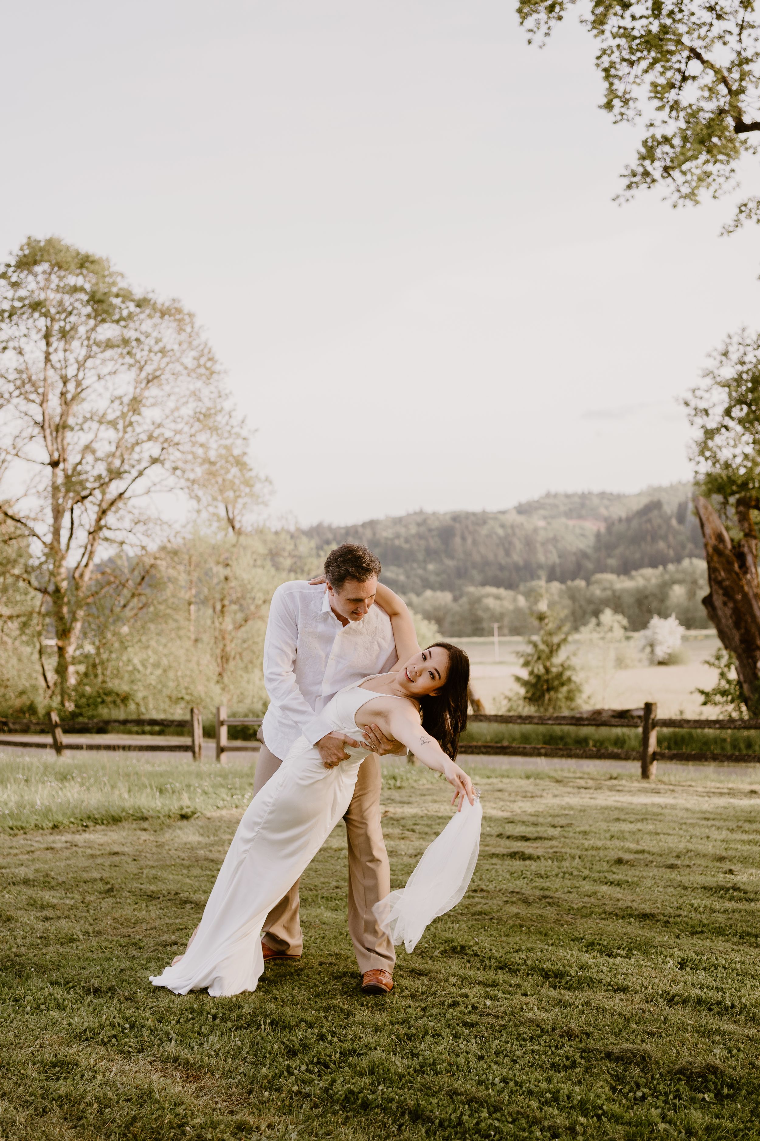 Couple in white clothing dancing together on a scenic grassy hillside.