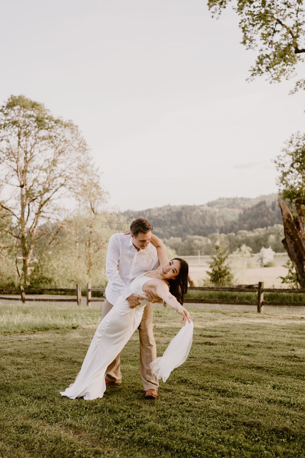 Couple in white clothing dancing together on a scenic grassy hillside.