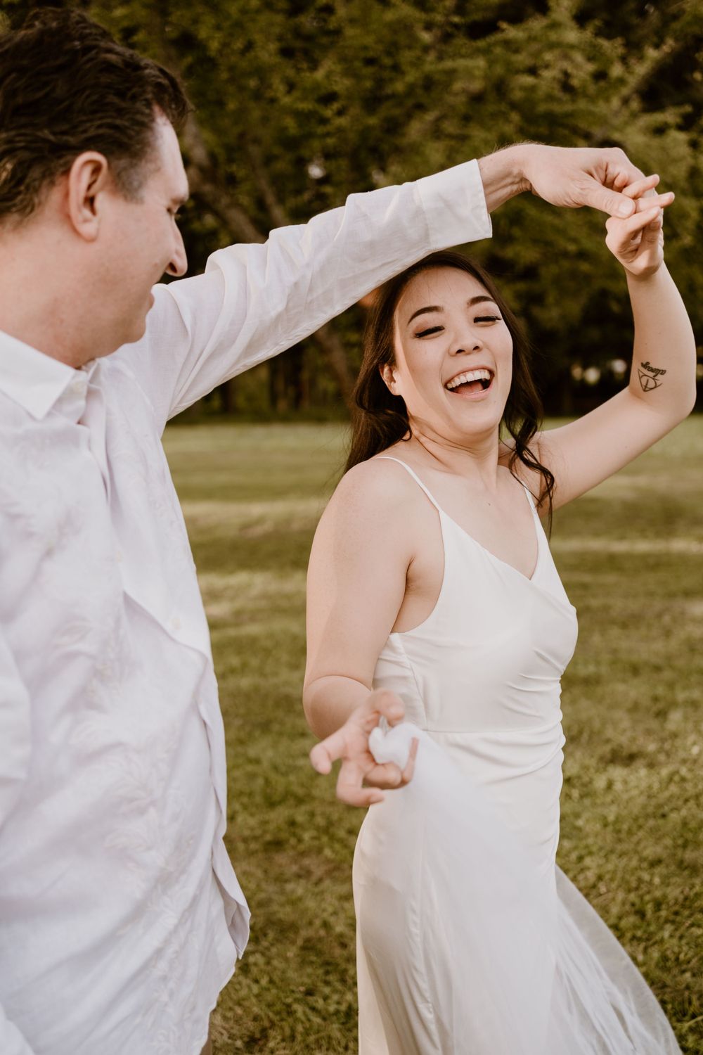 A joyful couple dances together on grassy grounds during their wedding day.