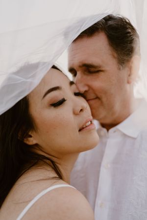 Intimate close-up moment between two people under a white veil.