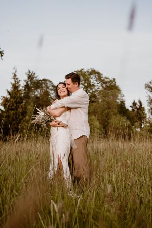 A romantic couple embraces in a golden field of tall grass during sunset.