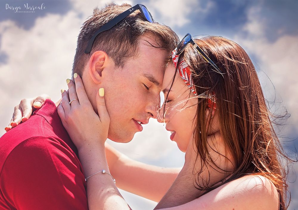 Intimate close-up of couple with sunlit sky in background.