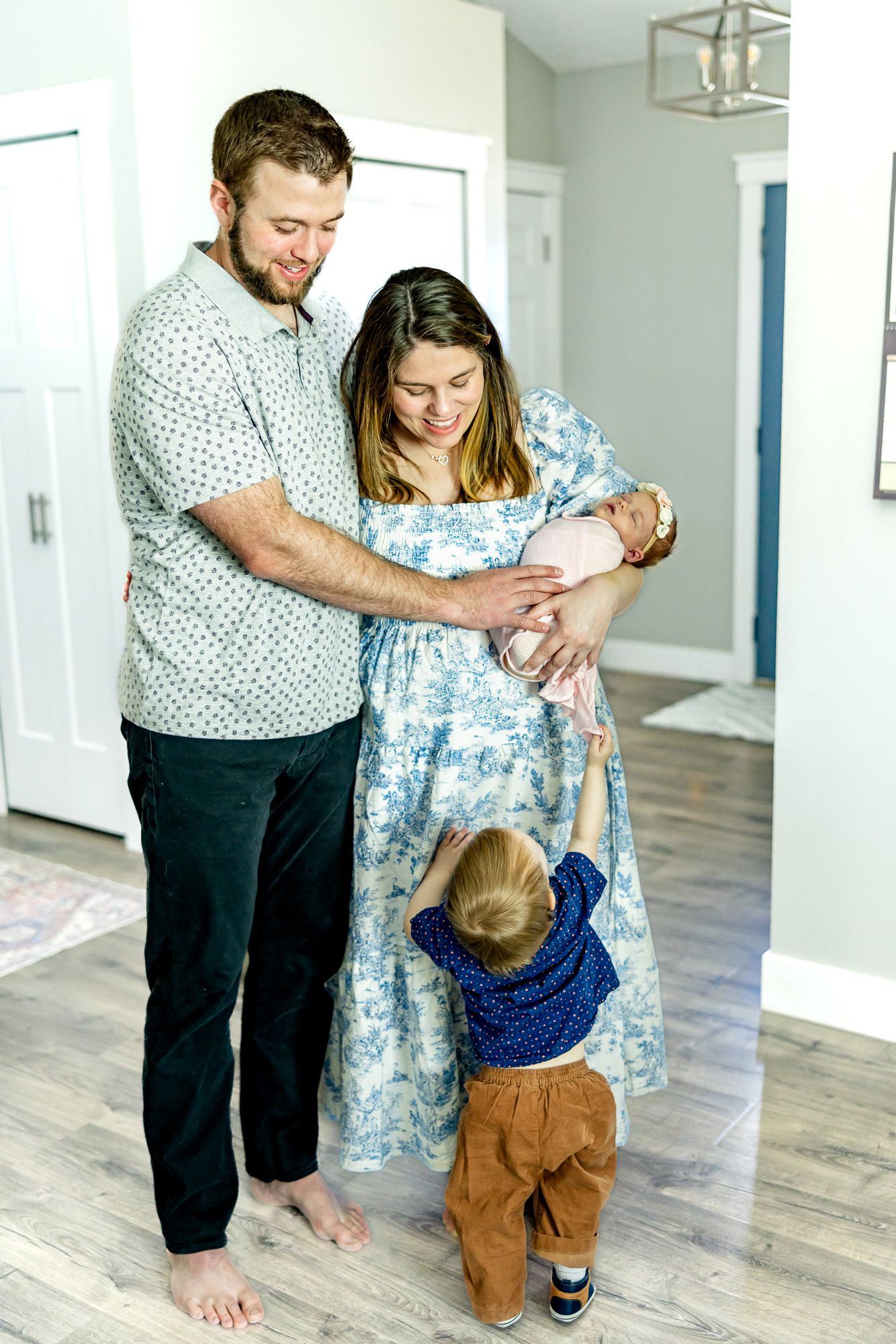 Toddler boy reaches towards his mom as parents hold his baby sister during lifestyle newborn photos in Colorado Springs.