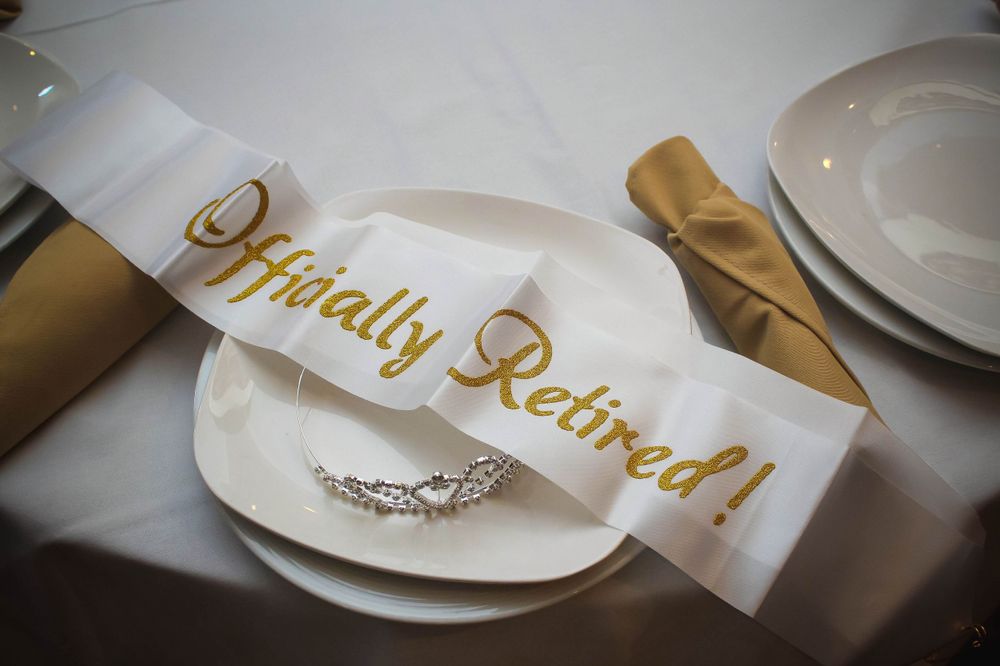 A table setting with a gold 'Officially Retired' sash and a ring on a white plate.