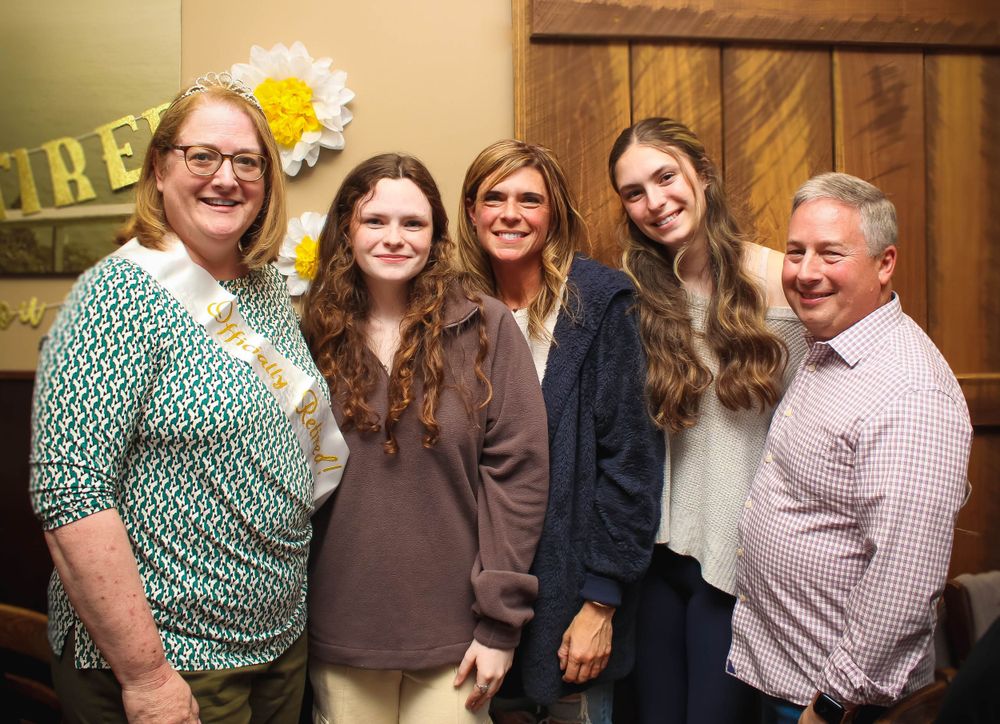 Group photo of five people at a celebration event with wooden paneling in the background.