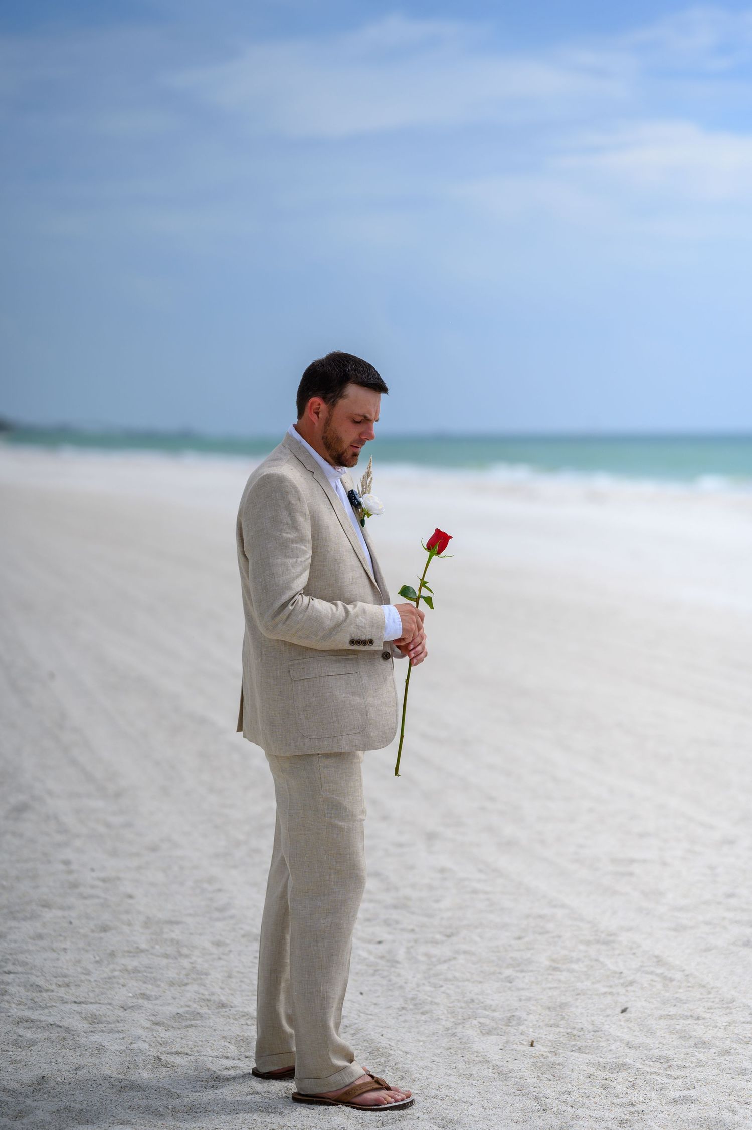 Groom holding a rose on a beach.