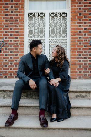 A couple sits together on brick steps wearing dark formal attire and sharing intimate moments.