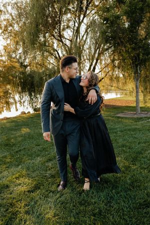 A couple in dark clothing embraces on grassy hill during golden hour.