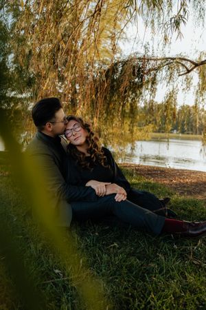 A couple shares romantic moments under willow trees by a lake during autumn.