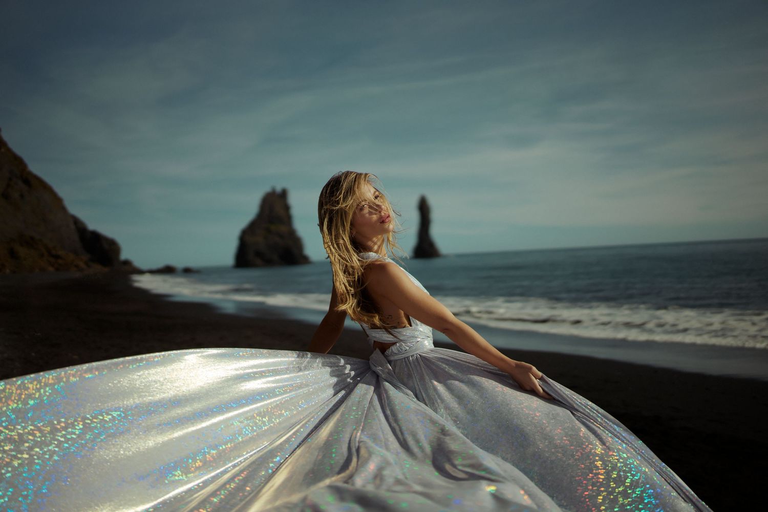 Flowing dress catches light on black sand beach with sea stacks in background.