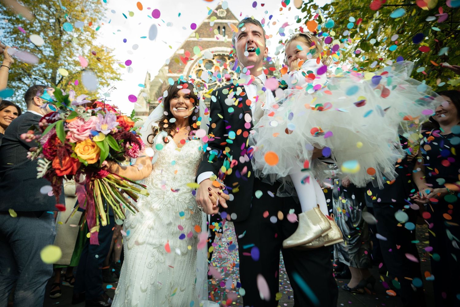 bride and groom are showered with colourful paper confetti as they leave church