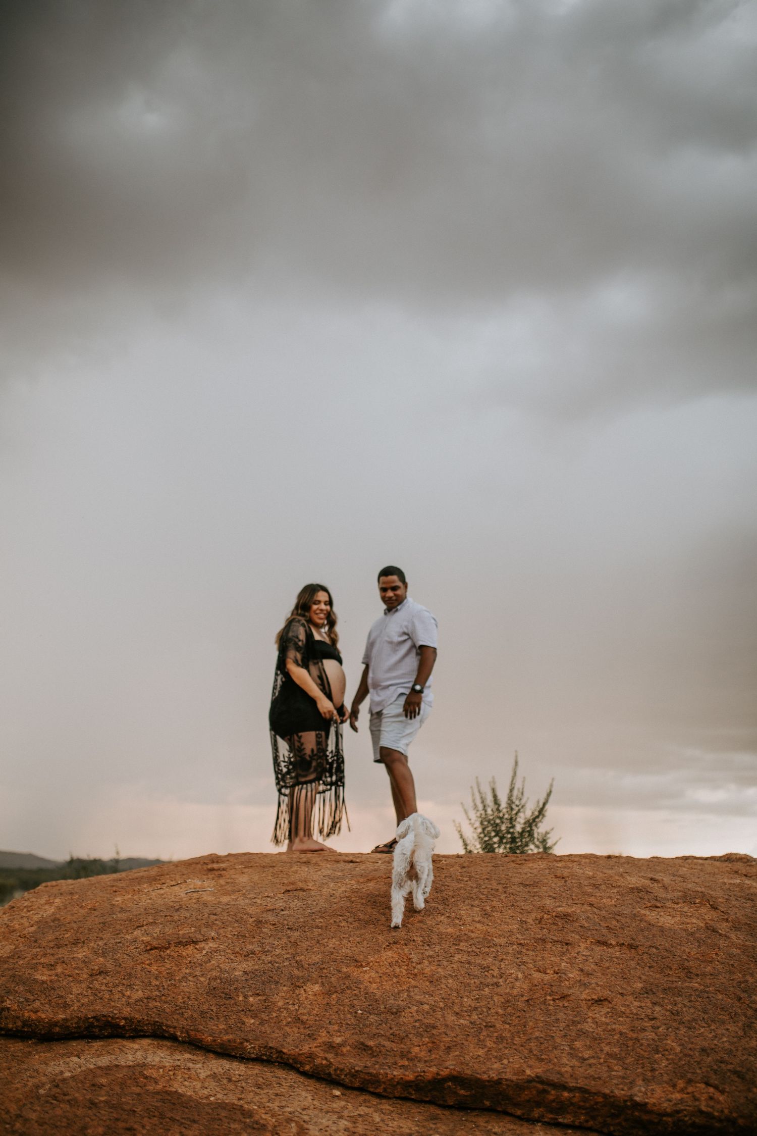 Beautiful mama to be poses on a hill at Granite Mines, Mount Isa holding hands with partner