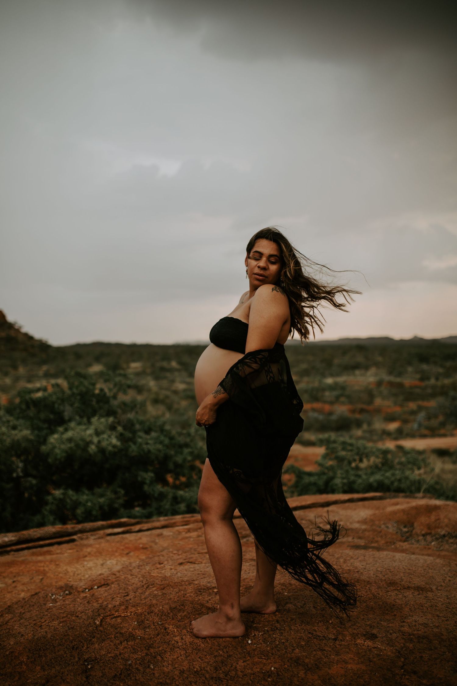 Beautiful mama to be poses on a hill at Granite Mines, Mount Isa with wind in her hair