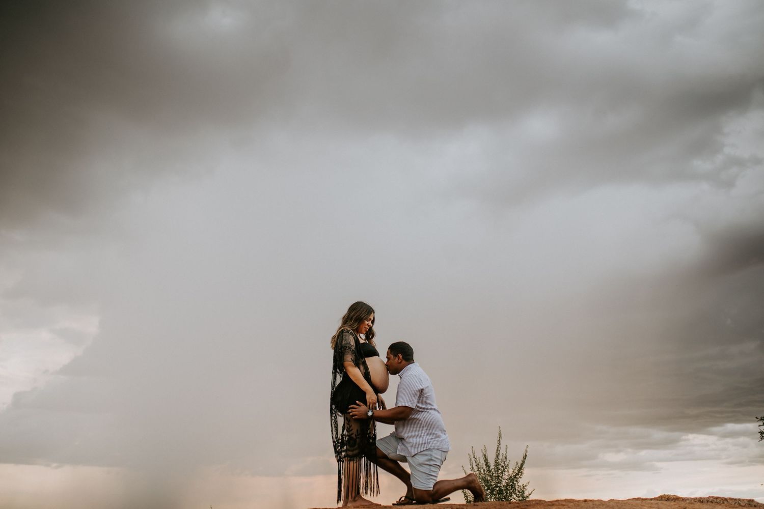 Beautiful mama to be poses on a hill at Granite Mines, Mount Isa as partner kisses belly