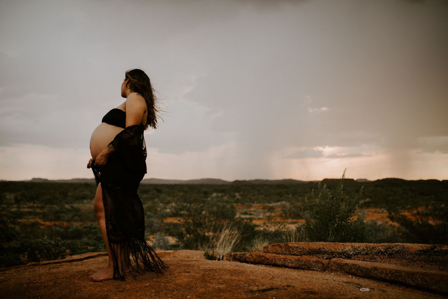 Beautiful mama to be poses on a hill at Granite Mines, Mount Isa
