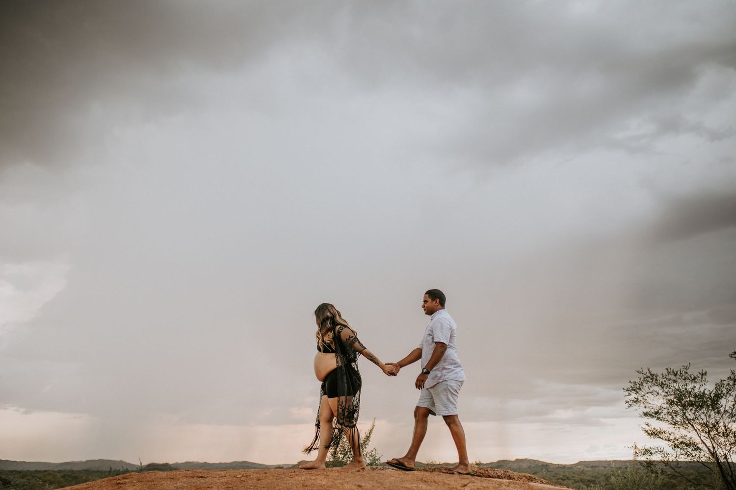 Beautiful mama to be walks on a hill at Granite Mines, Mount Isa holding her partners hand
