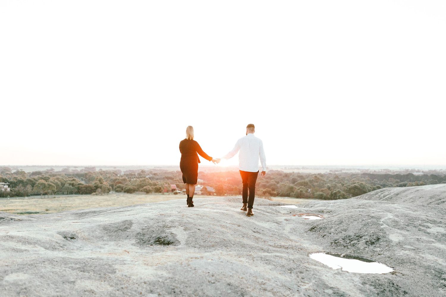 Two silhouettes walking together on a rocky landscape at sunset.