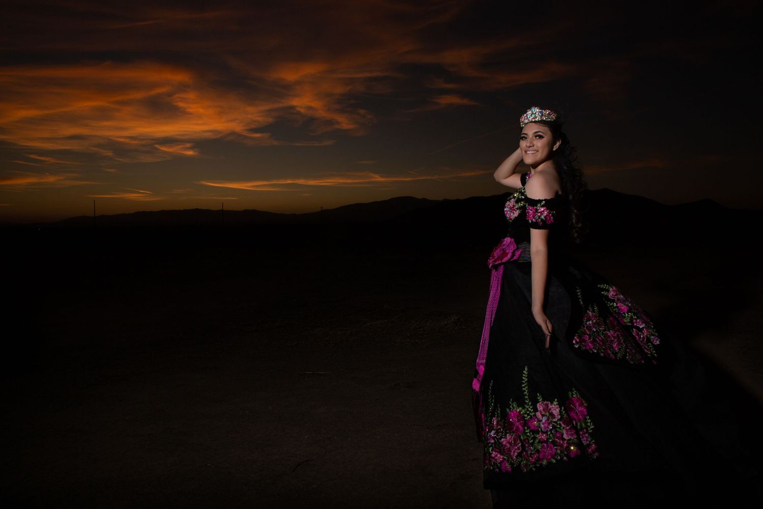 A silhouetted figure in a flowing dress stands against a dramatic orange and black sunset sky.