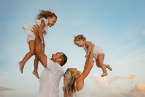 Joyful family plays and lifts children in the air against blue sky.