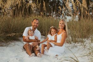 A family sits together on white sand dunes with tall beach grass at sunset.