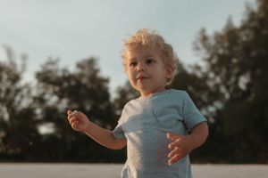 A small child in a light blue shirt looks up at the sky during golden hour.