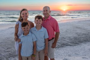 Family poses together on white sandy beach at sunset with ocean waves in background.