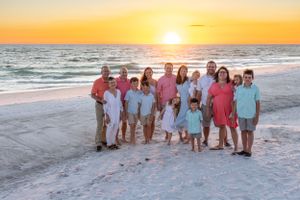 Large family group poses together on beach during golden sunset.