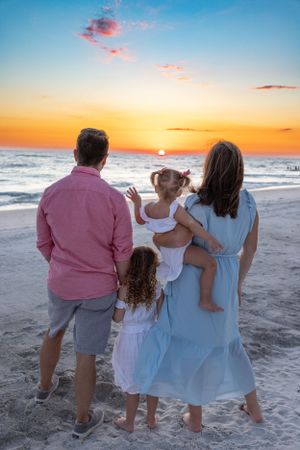 Group watches beautiful orange sunset over ocean waves while standing on beach.