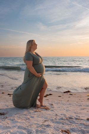 Maternity beach portrait with expectant mother in flowing dress during golden hour.